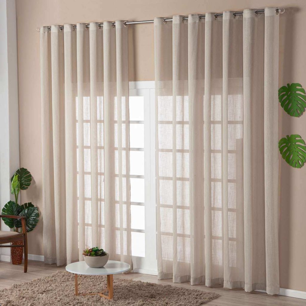 Foto que ilustra matéria sobre tipos de cortina mostra o detalhe de uma porta de madeira com vidro coberta por uma cortina de voal branca que deixa entrar a luz.
