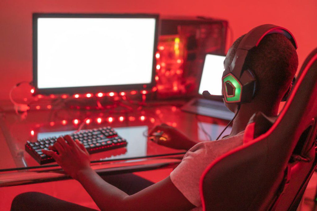 Jovem gamer jogando na estação usando computador desktop e laptop.