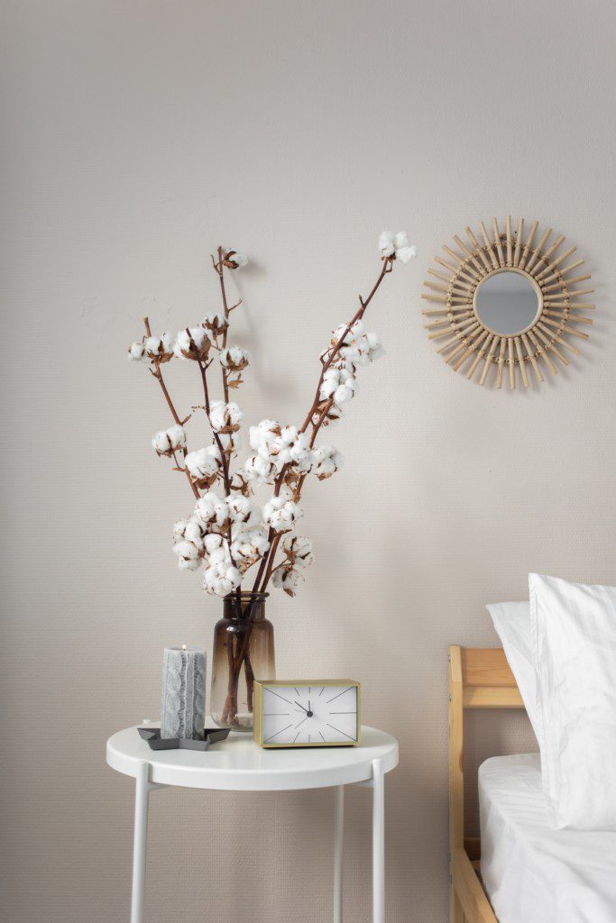Mesa de cabeceira branca em ferro, vaso com flores secas, vela e relógio.