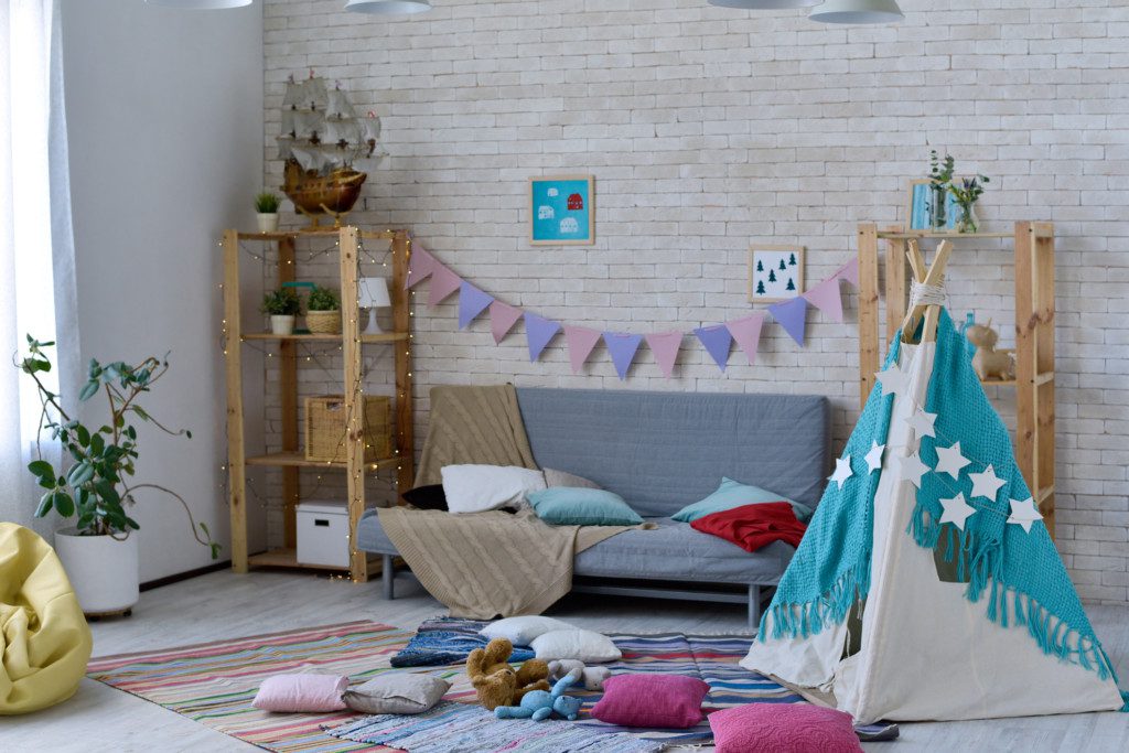  Imagem que ilustra matéria sobre quarto de brinquedos mostra um quarto de brinquedos com tapete, sofá, e cabaninha 


