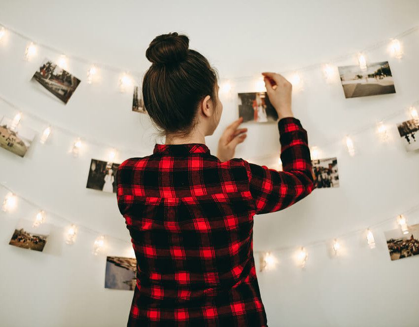 Foto que ilustra matéria sobre quarto tumblr mostra uma mulher pendurando fotos em um varal de luzes em uma parede