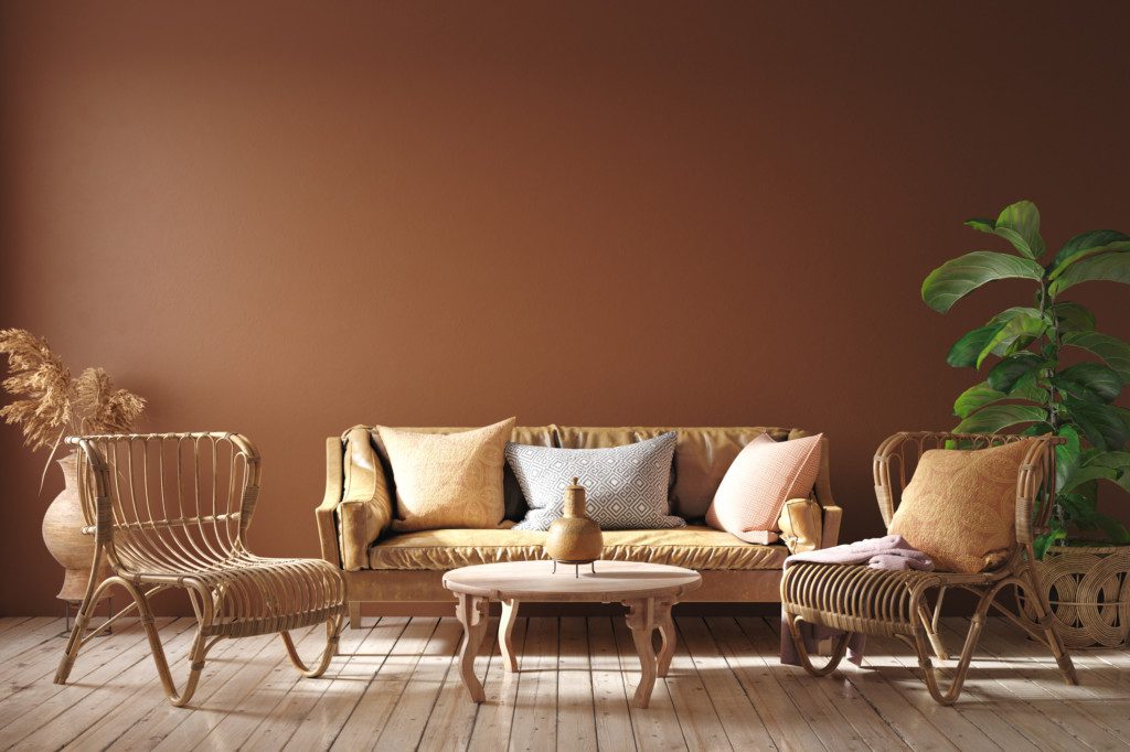 Foto de um ambiente com uma parede em em cor terracota em destaque. Além de sofá de couro, poltronas de vime e plantas.