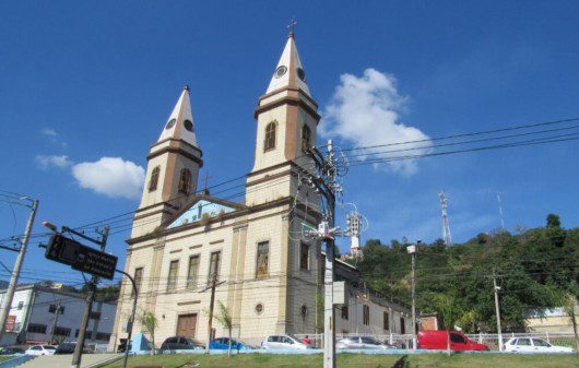 Foto que ilustra matéria sobre bairros de São Gonçalo mostra uma igreja com árvores e um céu azul ao fundo