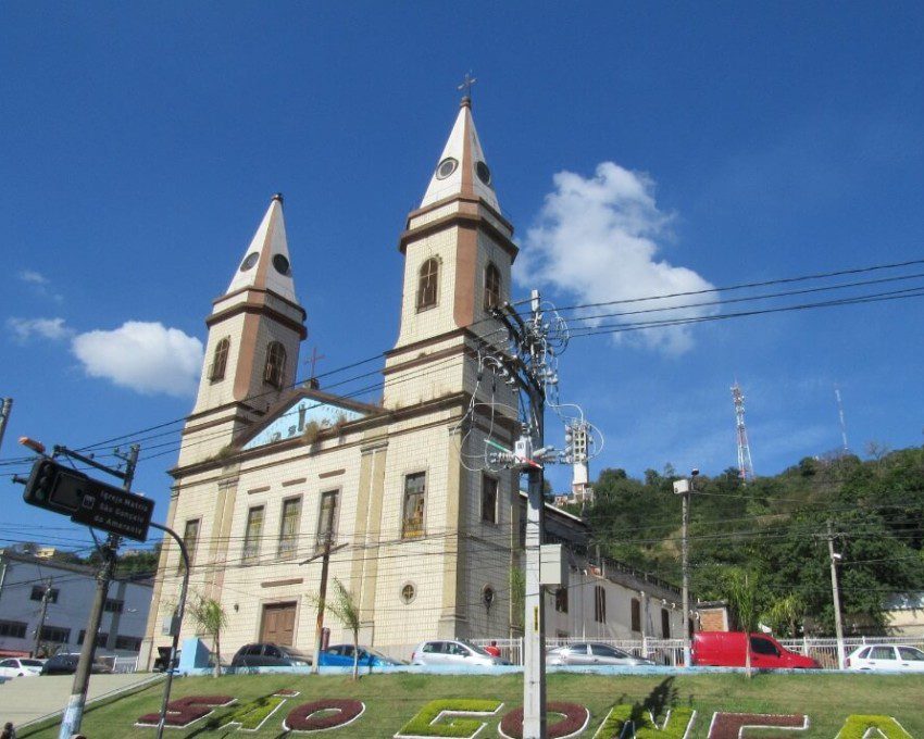 Foto que ilustra matéria sobre bairros de São Gonçalo mostra uma igreja com árvores e um céu azul ao fundo