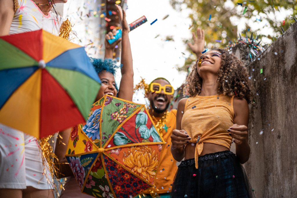 Amigos se divertindo no carnaval em casa com confete, fantasias e guarda-chuva do frevo. 