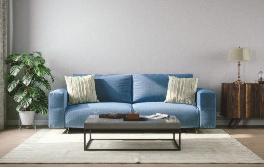 Imagem de um sofá azul na sala de estar com uma planta lateral.
