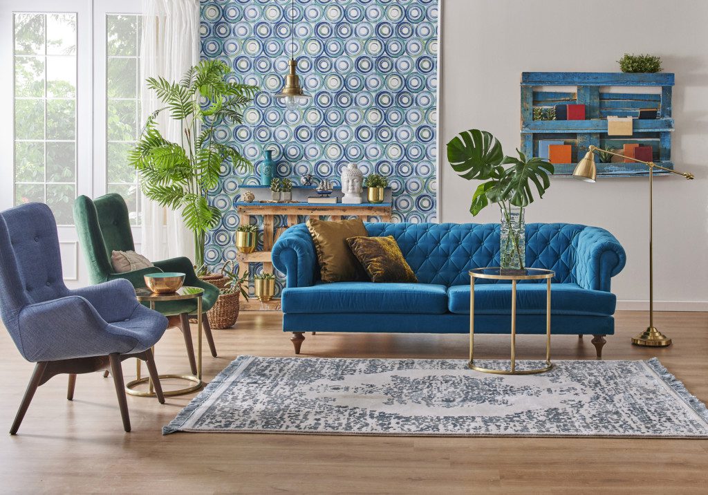 Sala de estar moderna com sofá azul retrô, poltronas e muitas plantas.