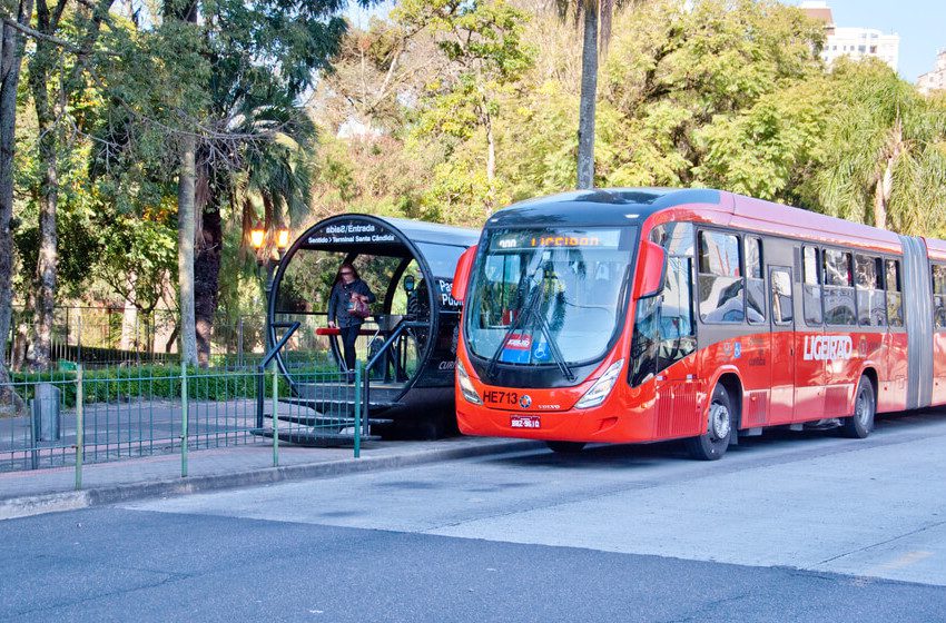 Foto que ilustra matéria sobre transporte público em Curitiba mostra uma estação do BRT com um ônibus biarticulado ao lado