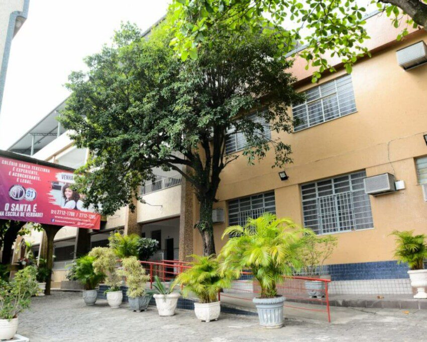 Foto que ilustra matéria sobre escolas em São Gonçalo mostra uma área interna do Colégio Santa Terezinha, com uma grande árvore diante de um prédio baixo