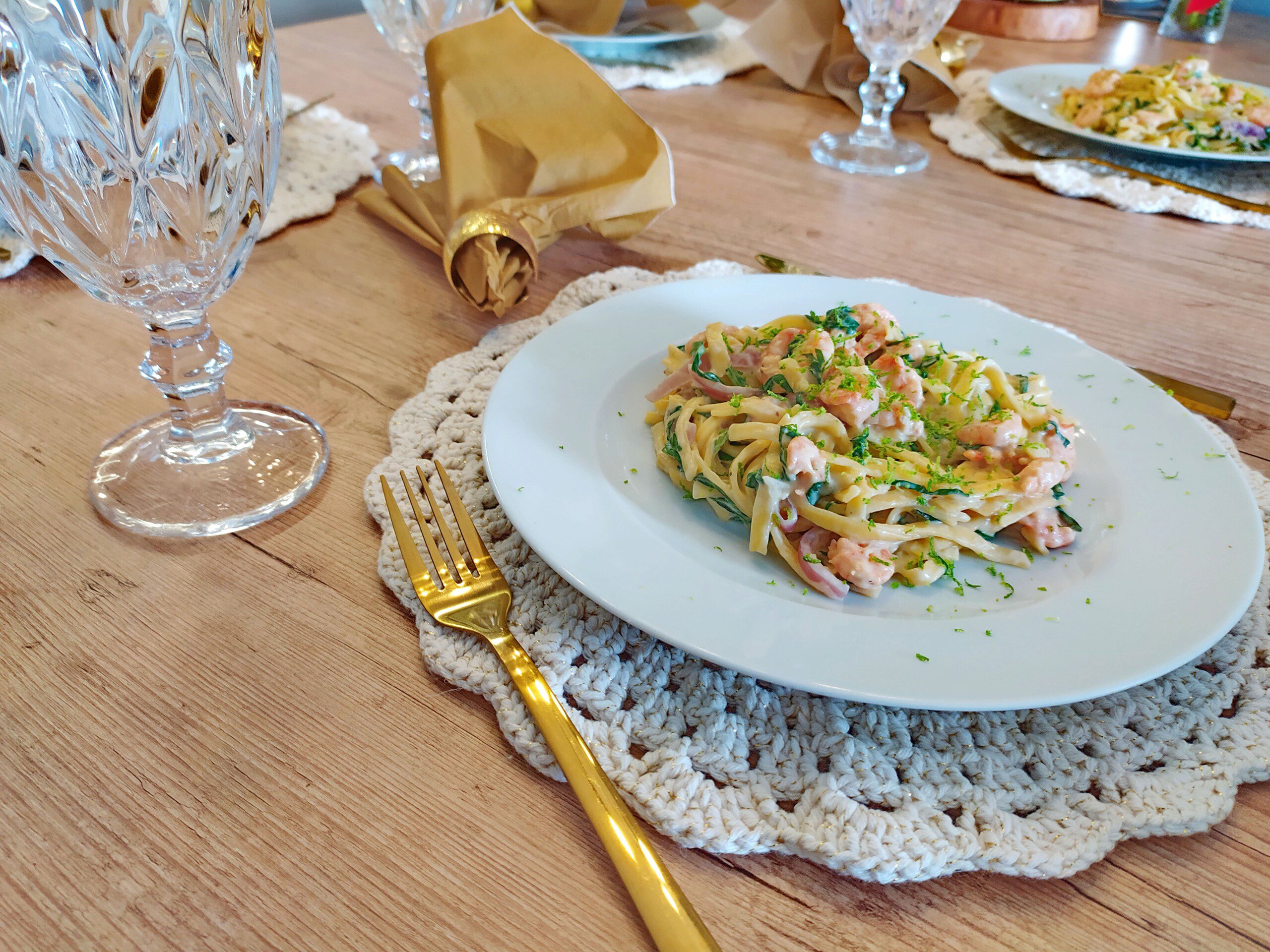 Sousplat de crochê em uma mesa posta clássica com talheres dourados e louça branca. 