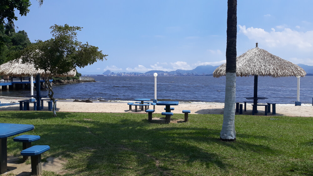 Foto que ilustra matéria sobre ilha no Rio de Janeiro mostra uma praia da Ilha do Governador com a Baía de Guanabara à frente e, ao fundo, as montanhas da cidade