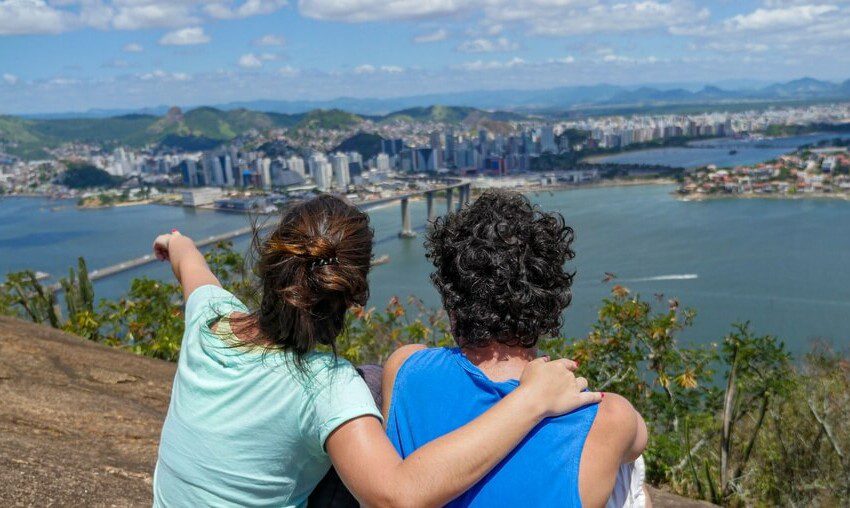 Foto que ilustra matéria sobre o Morro do Moreno mostra um casal sentado de costas olhando a vista da Baía de Vitória