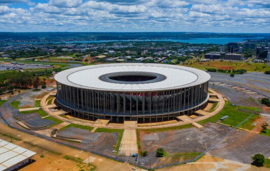 Foto que ilustra matéria sobre o Estádio Mané Garrincha mostra toda a arena vista de cima em um dia de céu azul