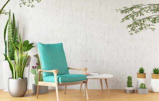 Imagem de uma poltrona verde com detalhes em madeira, mesa de apoio e muitas plantas.