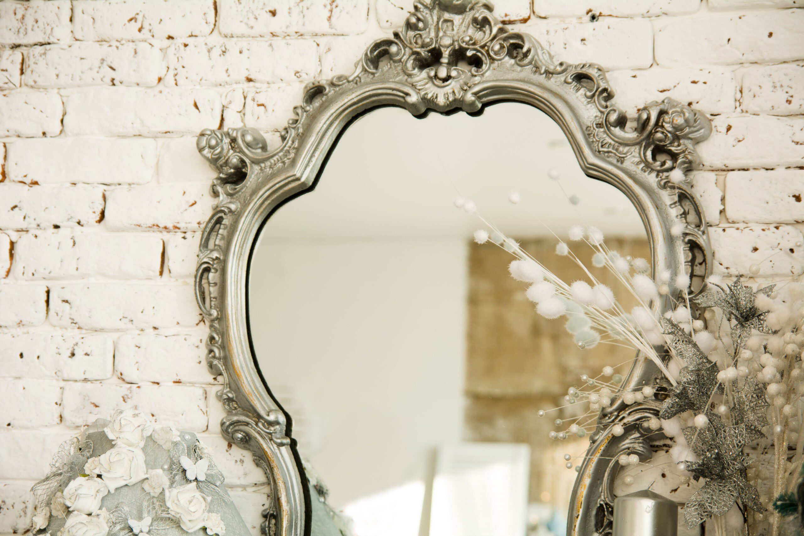 Imagem de um espelho prata em uma parede de tijolinhos. 