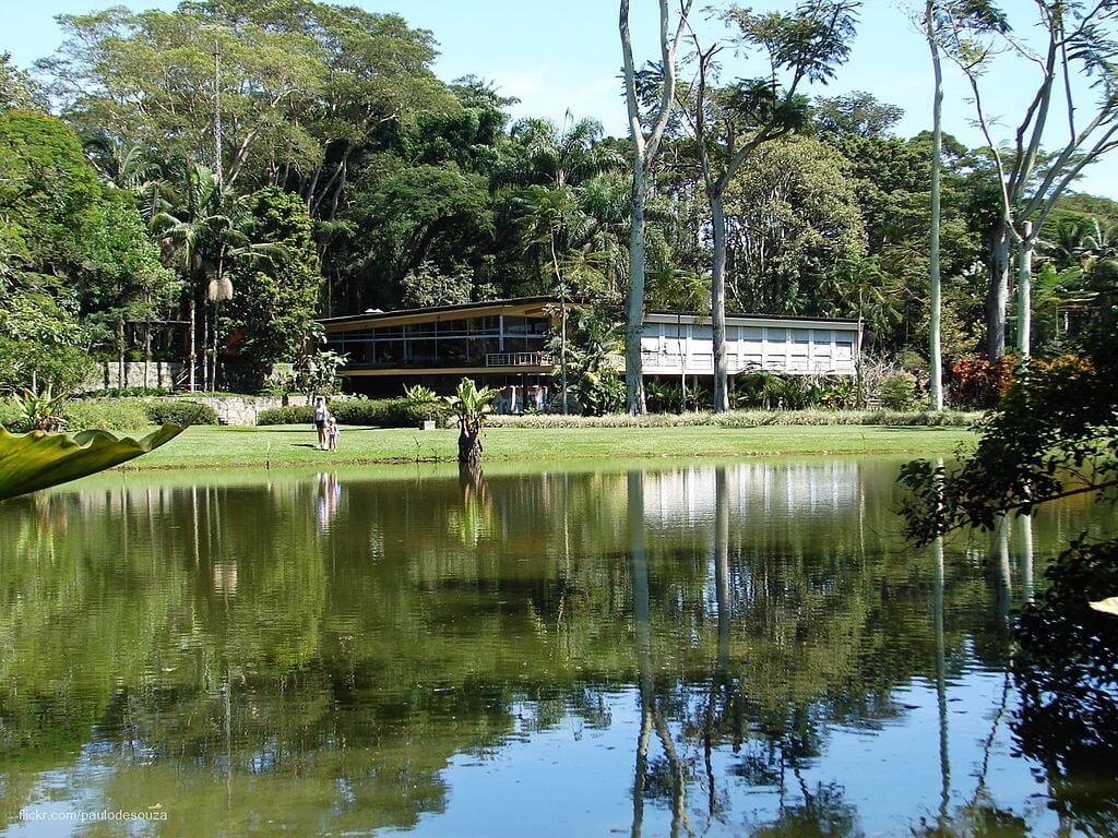 Foto que ilustra matéria sobre o Parque da Cidade em São José dos Campos mostra uma grande casa, a residência Olivo Gomes, ao fundo, com um lago em primeiro plano e muitas árvores em volta em um dia claro de céu azul.