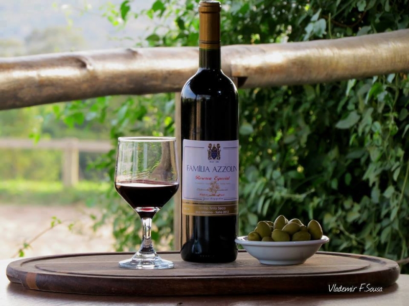 Garrafa de vinho ao lado de uma taça cheia, na Adega Azzolin Cantina e Restaurante.