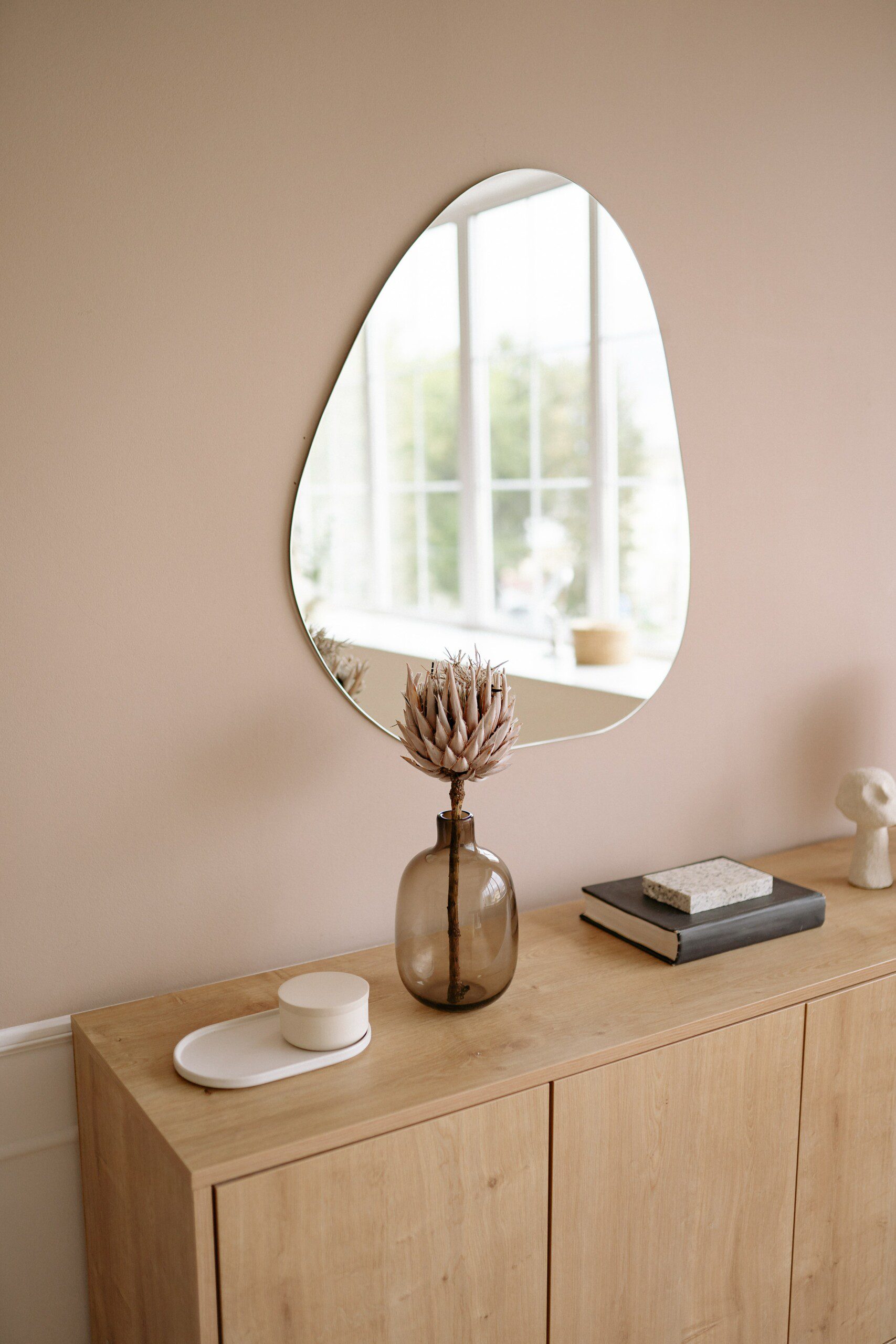 Aparador em madeira clara, com itens decorativos em cima e um espelho. 