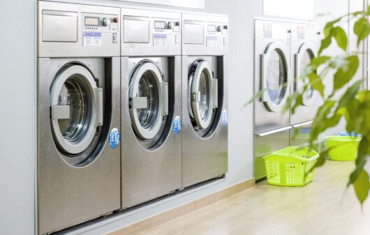 Imagem de várias máquinas de lavar do estilo industrial em uma lavanderia.