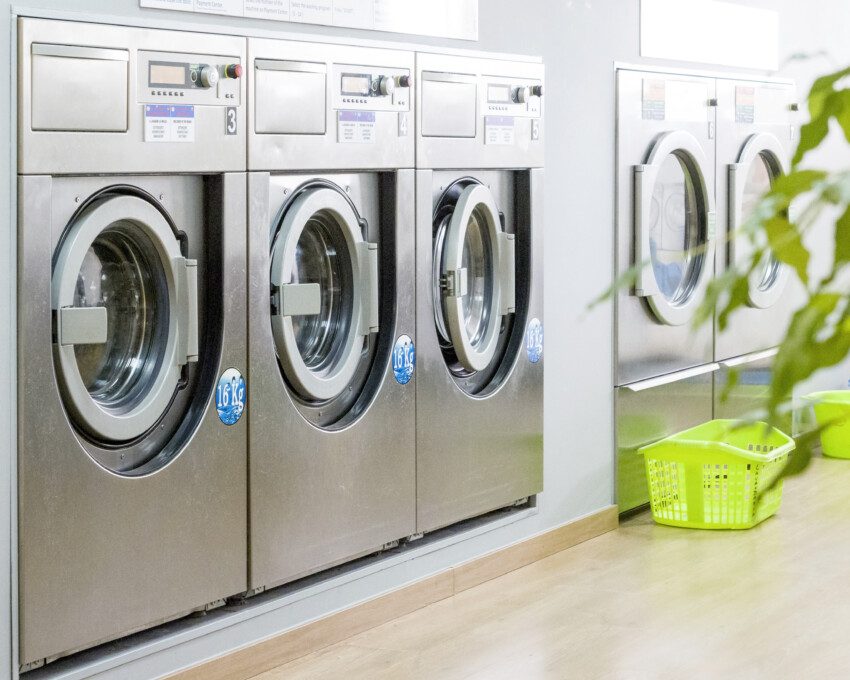 Imagem de várias máquinas de lavar do estilo industrial em uma lavanderia.
