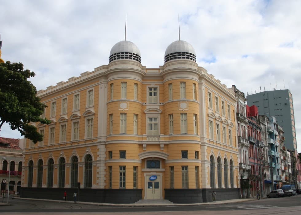 Fachada de uma prédio amarelo, com detalhes em branco, em uma esquina. O prédio é da Caixa Cultural de Recife.