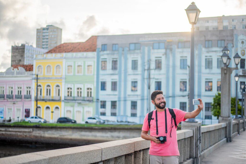 Visitante tira fotografias de si com prédios do Centro Histórico de Recife ao fundo.
