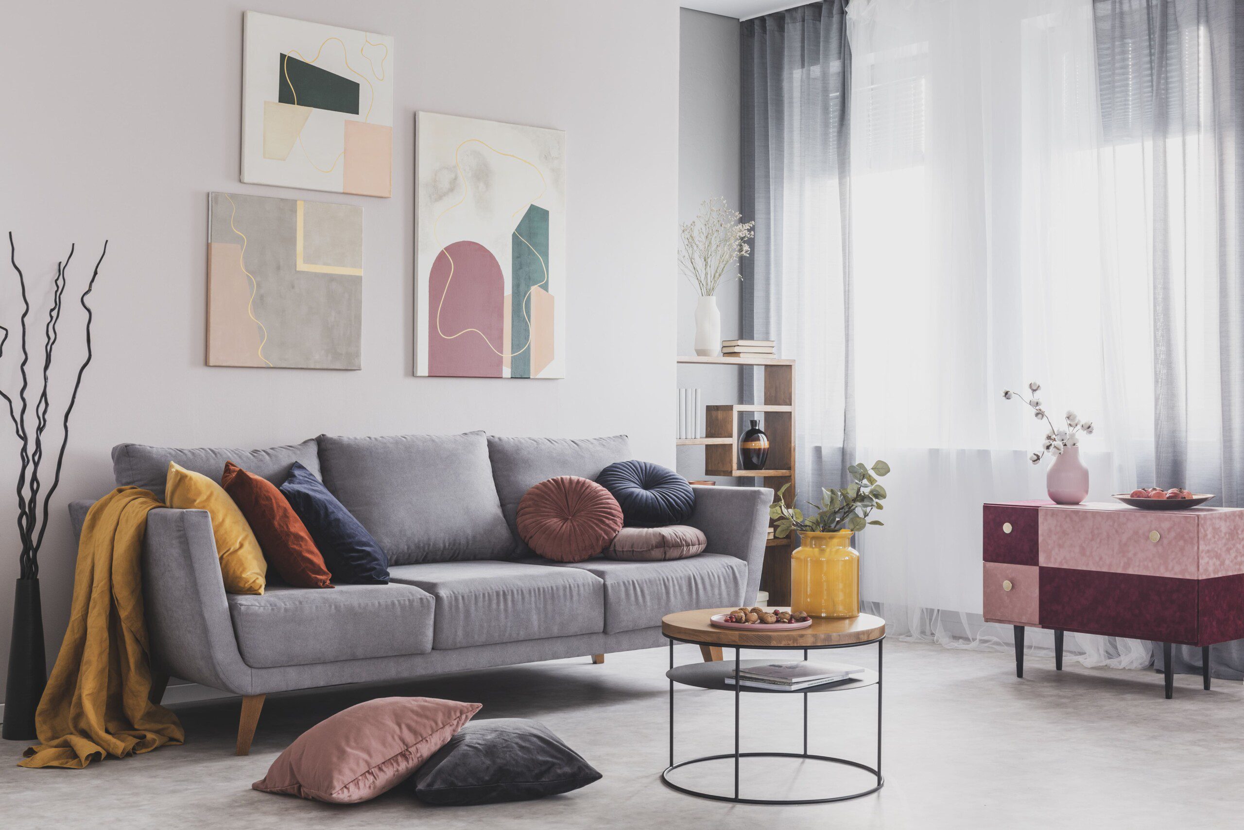 Sala de estar com quadros atrás do sofá cinza, almofadas coloridas e decoração moderna. 