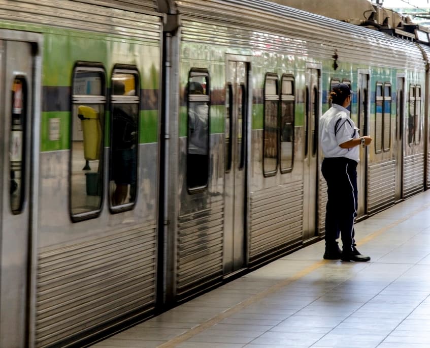 Imagem dos vagões do metrô de Recife parados na estação. Há também um guarda ao lado do vagão.