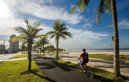 Foto que ilustra matéria sobre o que fazer em Praia Grande mostra um ciclista pedalando na ciclovia da orla de uma das praias da cidade