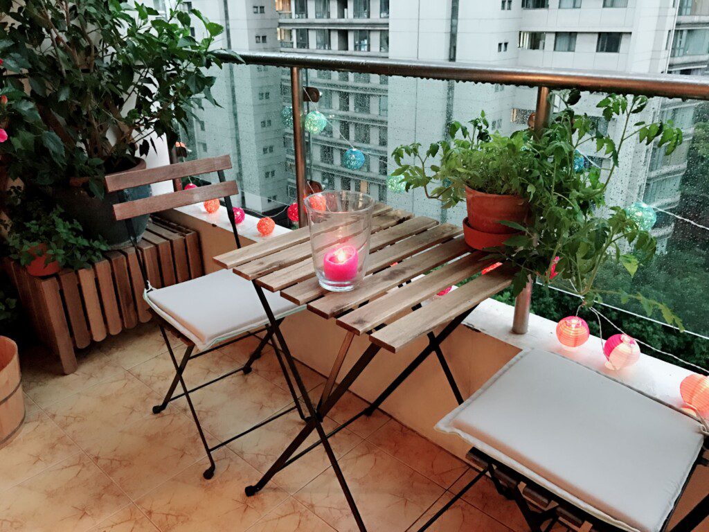 Varanda com plantas e um conjunto de mesa e duas cadeiras em madeira. 