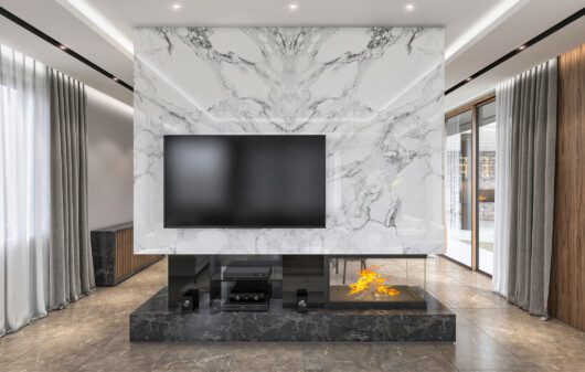 Sala de estar com TV, lareira e um painel com efeito marmorizado.