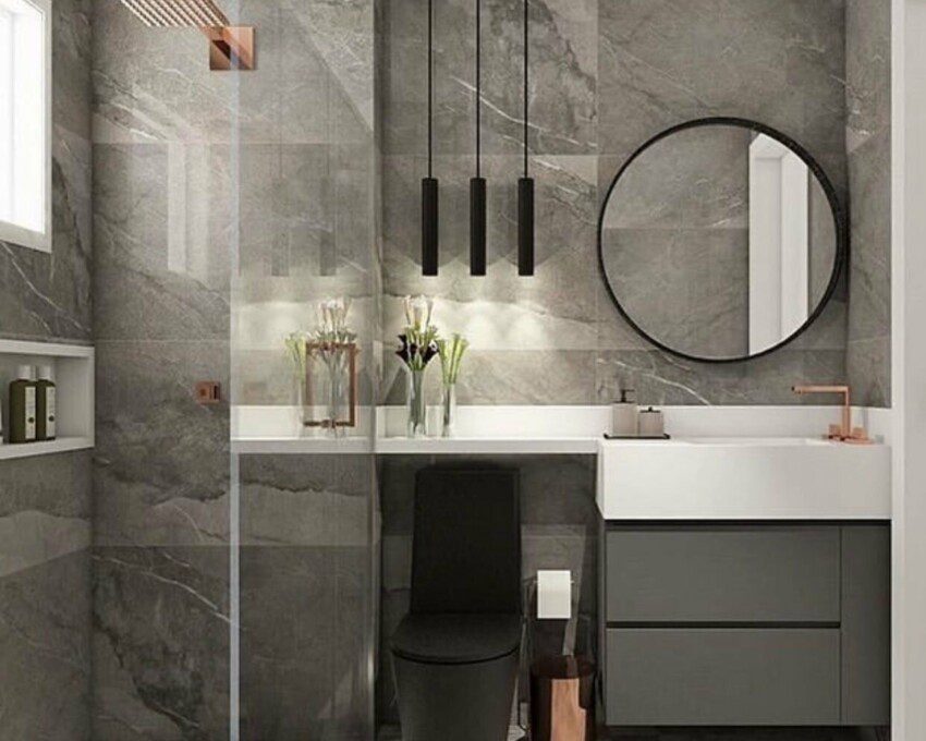 Banheiro cinza com revestimento em mármore, luminária pendente, espelho redondo e vaso preto.