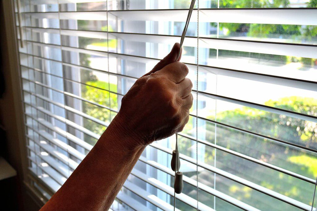 Uma mão segura o cordão de controle de uma persiana estilo horizontal.