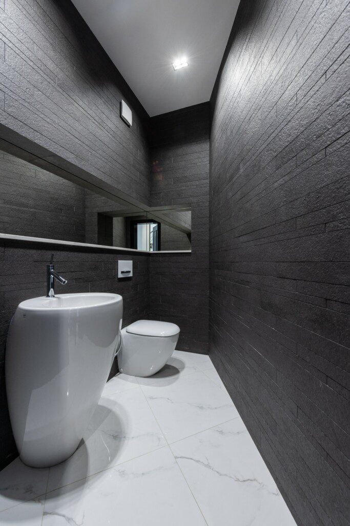 Banheiro com revestimento em cinza escuro com tijolinhos e louças em cerâmica branca. 