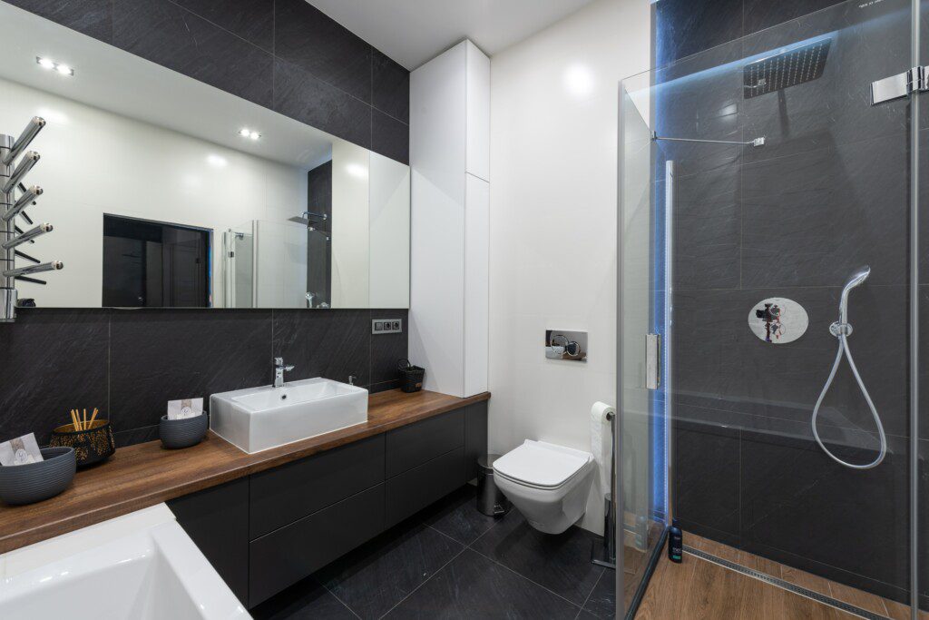 Banheiro com cinza escuro, paredes na cor branca e superfície da pia em madeira. 