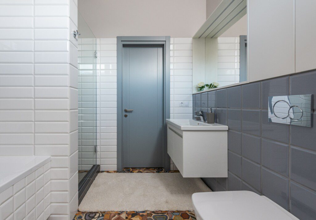 Banheiro com revestimento cinza, espelho grande e armários e louças na cor branca. 