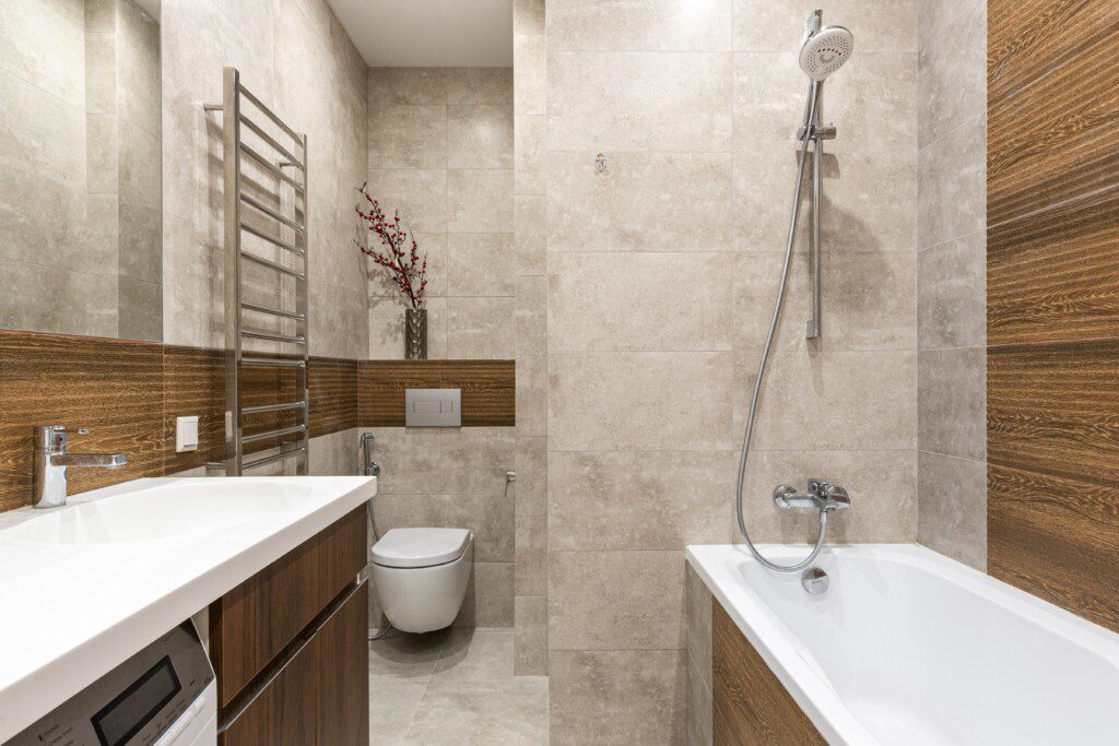 Banheiro bege com detalhes em madeira e revestimento clean. 