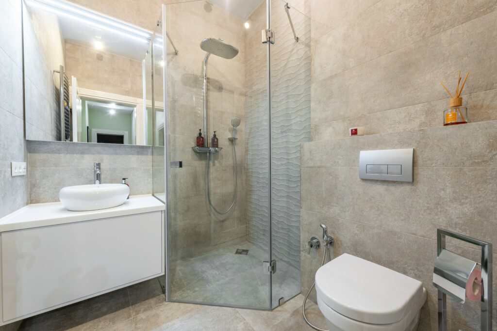 Banheiro com revestimento bege, móveis brancos e acessórios em prata. 