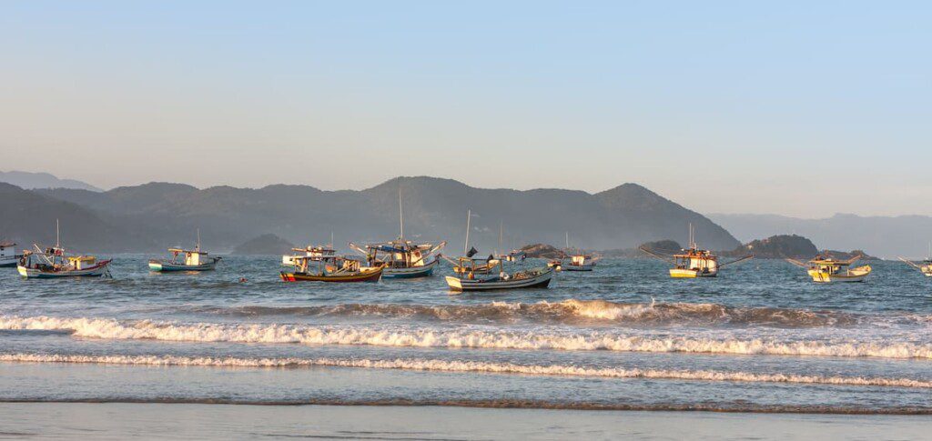 Foto da paisagem marítima da Praia do Perequê, com vários barcos próximos a faixa do areia.