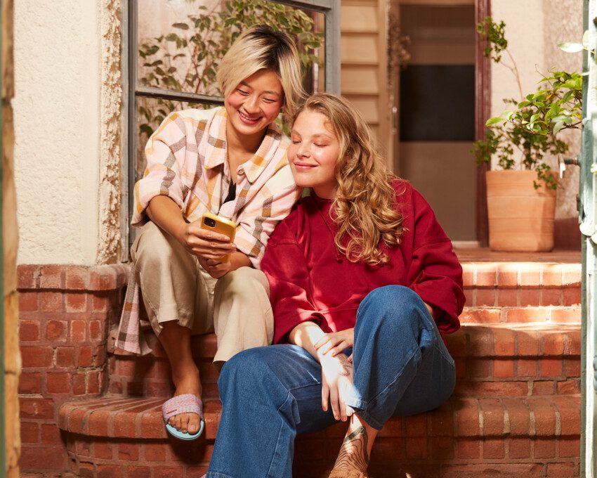 Foto que ilustra matéria sobre como fazer renda extra mostra duas meninas olhando para o celular e felizes