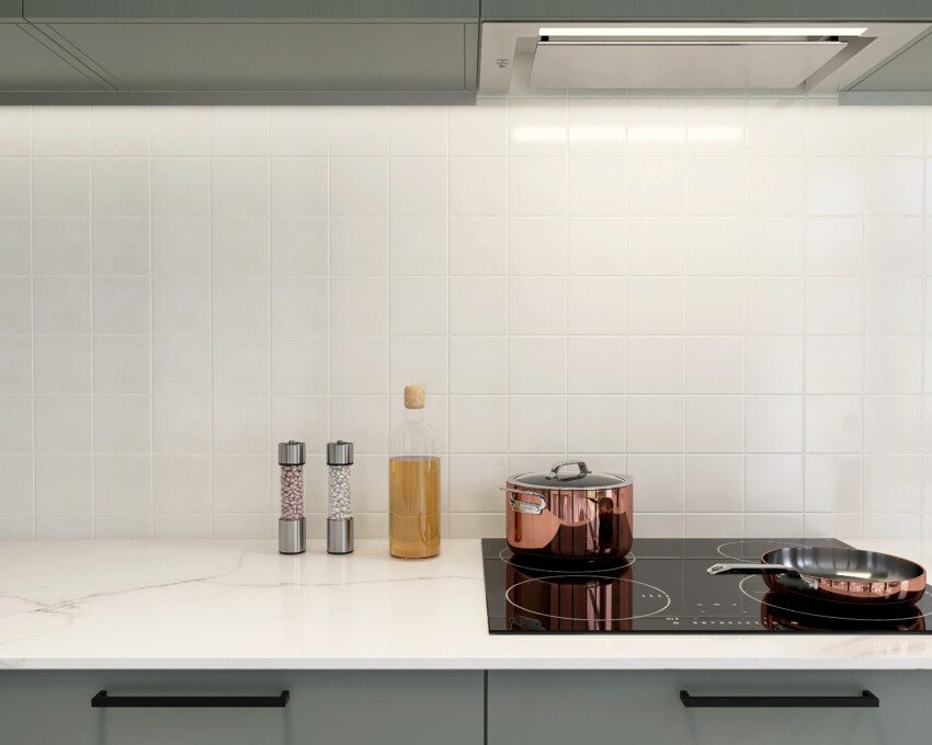 Imagem de um backsplash revestido de azulejo branco por trás de um balcão branco com cooktop, panelas e temperos