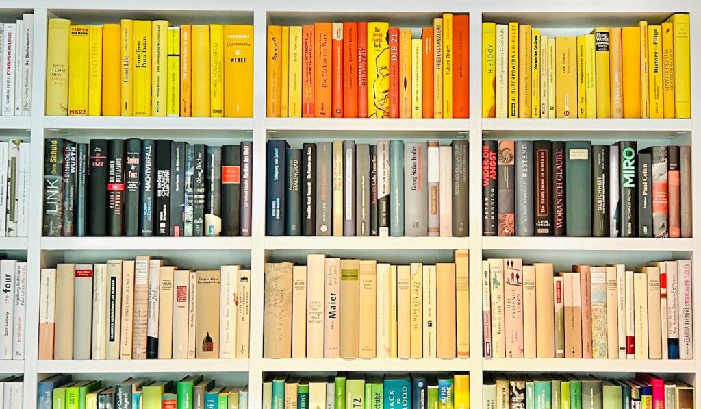 Livros, em uma estante, organizados por cor.