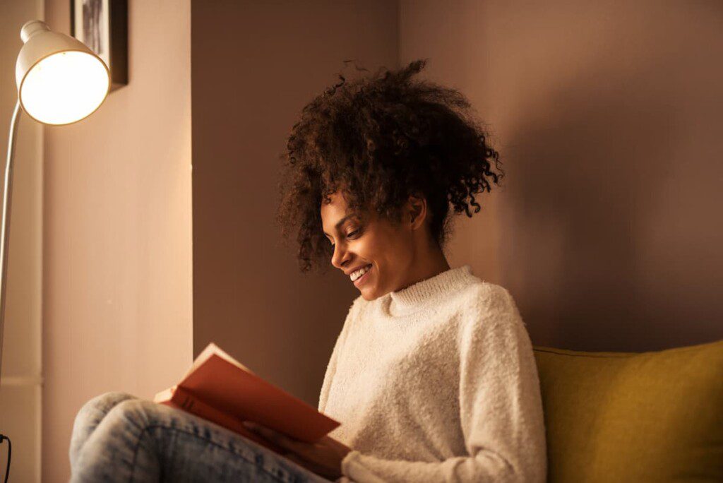 Uma mulher ler um livro em seu cantinho de leitura com auxílio da luz de uma luminária de chão.