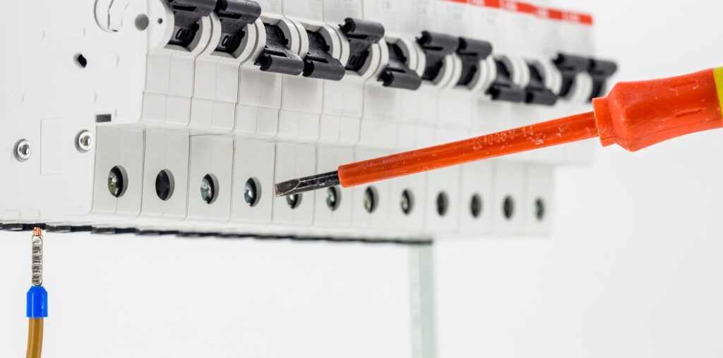 Imagem de um dispositivo elétrico com interruptores em um fundo branco e uma chave de teste com cabo laranja próximo a eles