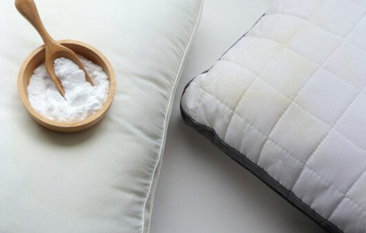 Foto que ilustra matéria sobre como lavar travesseiro mostra dois travesseiros, sendo que um deles tem em cuma uma pequena vasilha com uma colher de madeira e cheia de bicarbonato de sódio.
