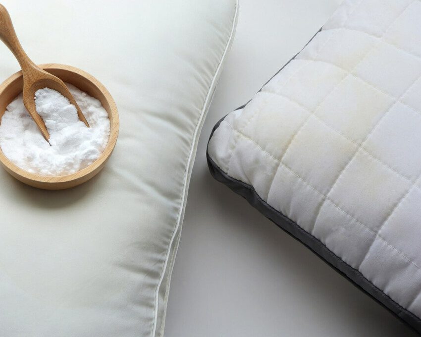 Foto que ilustra matéria sobre como lavar travesseiro mostra dois travesseiros, sendo que um deles tem em cuma uma pequena vasilha com uma colher de madeira e cheia de bicarbonato de sódio.