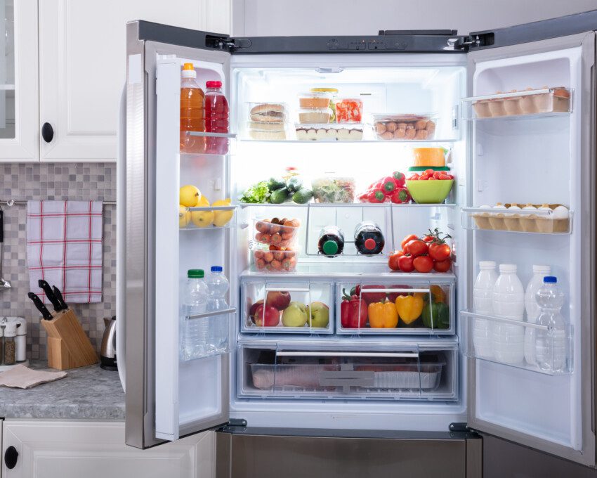 Imagem de uma geladeira inox aberta cheia de alimentos diversos ao lado de armários