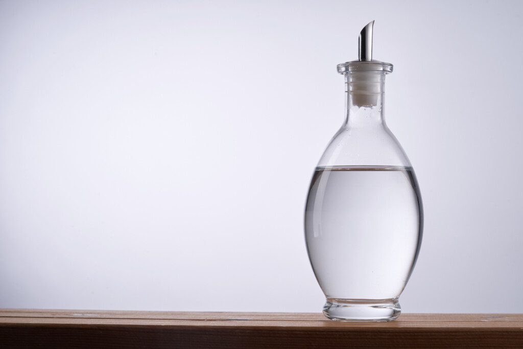 Imagem de um recipiente transparente com a ponta metálica com vinagre branco contra um fundo acinzentado 