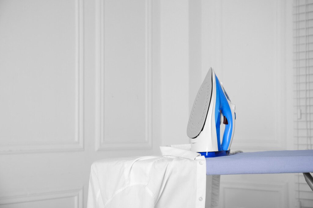 Imagem de ferro seco ao lado de uma camisa branca sobre uma tábua de passar roupa azul