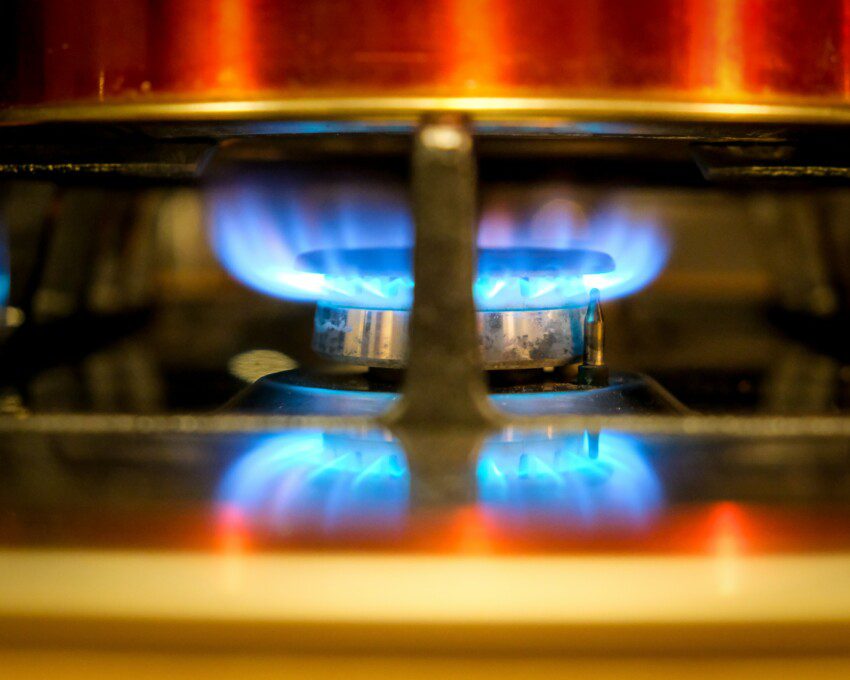 Imagem com zoom de uma boca de fogão com a chama acesa.